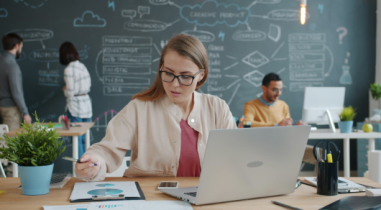 Woman Sitting at a Desk and Working on a Laptop